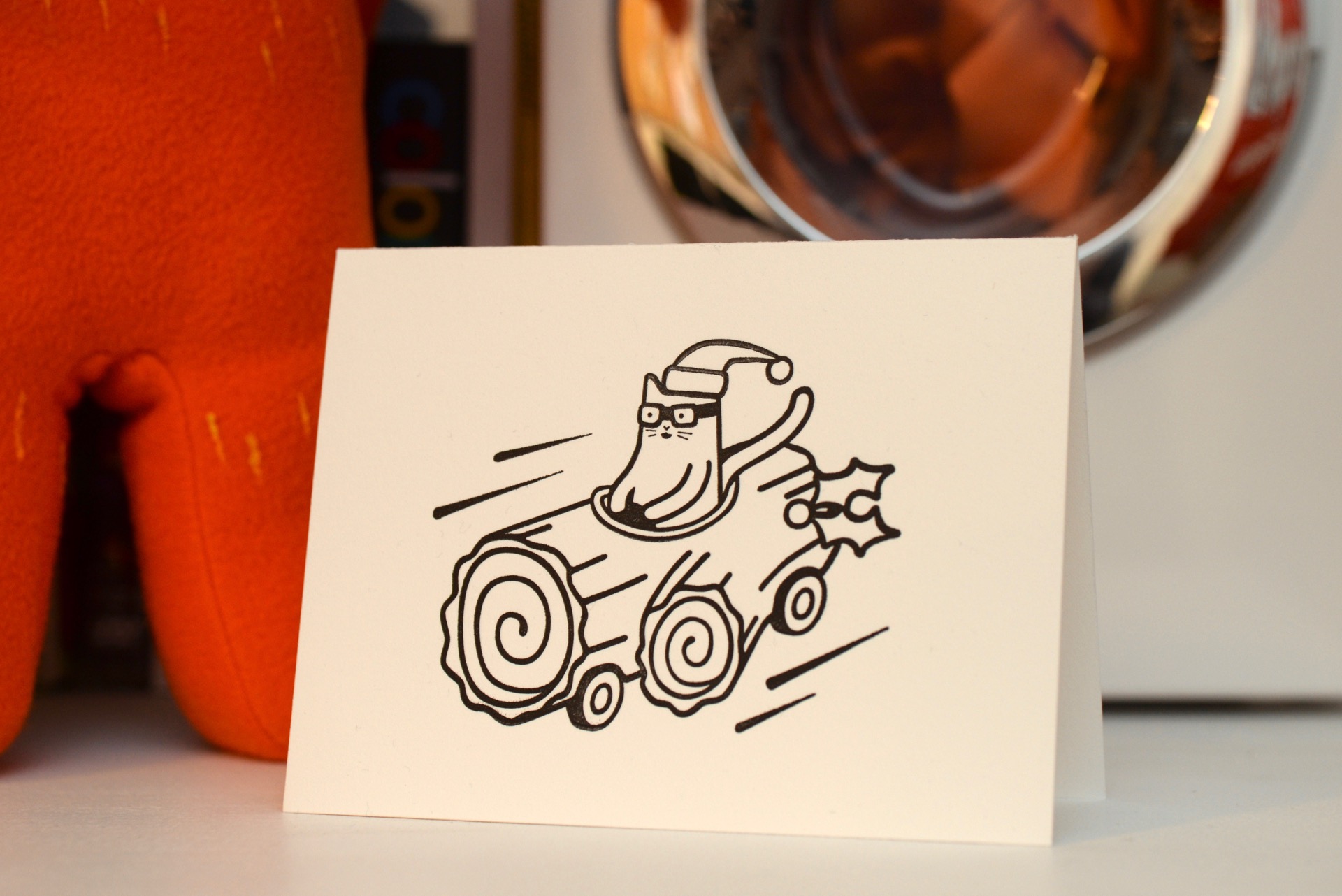 Hand-letterpressed Christmas card featuring Asta the cat driving a motorised Yule Log